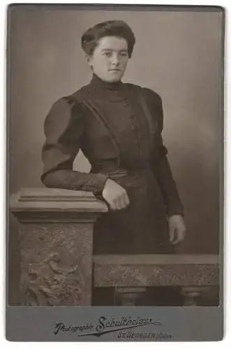 Fotografie Schultheiss, St. Georgen, Portrait einer Frau in dunklem Kleid mit architektonischem Detail im Hintergrund