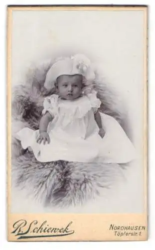 Fotografie R. Schienvek, Nordhausen, Töpferstr. 1, Baby in weissem Kleid auf Pelzdecke