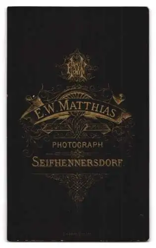 Fotografie E.W. Matthias, Seifhennersdorf, Portrait eines jungen Mannes in Anzug neben kunstvoll verziertem Podest