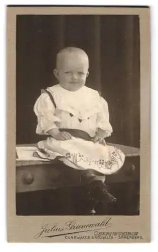 Fotografie Julius Grunewald, Oberneukirch, Kleinkind sitzend auf einem Tisch