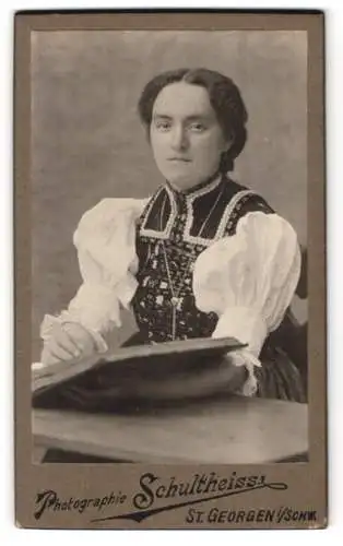 Fotografie Atelier Schultheiss, St. Georgen, Frau in traditioneller Tracht mit Buch