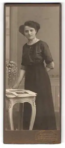 Fotografie Hermann Luh, Seifhennersdorf, Frau in elegantem Kleid neben einem Tisch mit Blumen