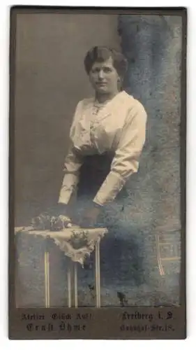 Fotografie Ernst Öhme, Freiberg i. S., Bahnhof-Str. 18, Frau in eleganter Bluse neben Tisch mit Blumenschmuck