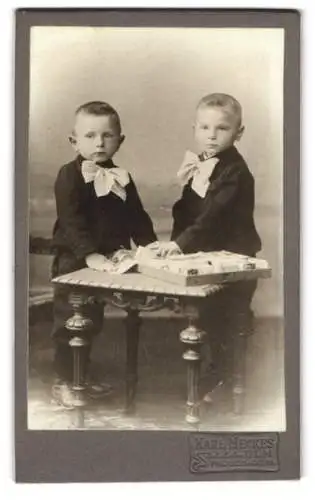 Fotografie Karl Meckes, Ulm, Promenade 19, Zwei Jungen mit grossen Schleifen an einem Tisch