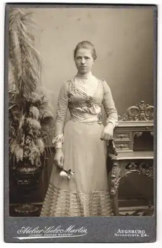 Fotografie Gebr. Martin, Augsburg, Bahnhofstrasse 24, Junge Dame in elegantem Kleid neben kunstvoll verziertem Tisch