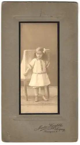 Fotografie Martin Herzfeld, Leipzig, Thomasgasse 4, Kleines Mädchen mit Schleife im Haar steht neben einem Stuhl