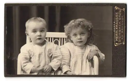 Fotografie Herm. Krausse, Steinbach / Erzgeb., Am Bahnhof, Zwei Kinder in weissen Kleidern auf einem Stuhl