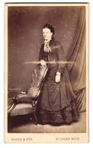 Fotografie Briggs & Son, St John`s Wood, 40 High Street, Frau in elegantem Kleid neben Stuhl