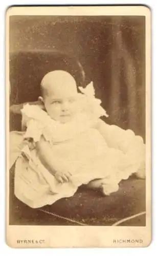 Fotografie Byrne & Co, Richmond, Hill Street, Sitzendes Baby in einem weissen Kleid