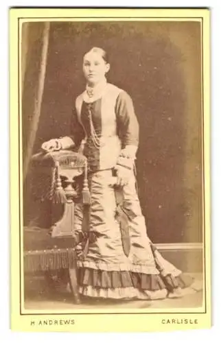 Fotografie H. Andrews, Carlisle, Sheffield St 46, Elegante Dame in viktorianischer Kleidung neben dekorativen Stuhl