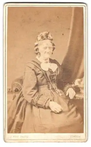 Fotografie J. Pitt, London, Bethnal Green Road, Sitzende ältere Dame in dunklem Kleid und Haube