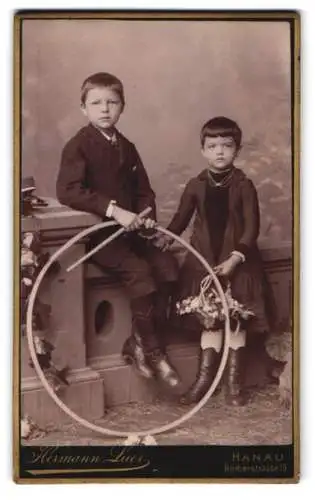 Fotografie Hermann Luer, Hanau, Römerstrasse 19, Zwei Kinder in traditioneller Kleidung mit Hula-Hoop-Reifen und Blumenst