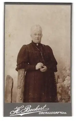 Fotografie H. Beckert, Oberaudorf a. Inn, Blumen und Holzstrukturen im Hintergrund, ältere Frau in dunklem Kleid