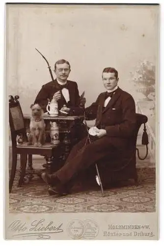 Fotografie Max Liebert, Holzminden a. W., Zwei junge Männer in Anzügen mit Pfeifen beim Skatspiel, Bierkrug und Hund