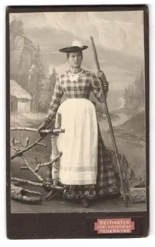 Fotografie J. Reitmayer, Tegernsee, Bürgerliche Frau in Tracht mit einem Wanderstab vor einer Studiokulisse