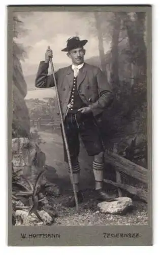 Fotografie W. Hoffmann, Tegernsee, Junger Mann in Tracht mit einem Wanderstab und Lederhose