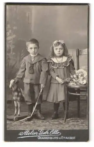 Fotografie Gebr. Otto, Oranienburg, Zwei Kinder mit Spielzeugpferd und Blumenstrauss