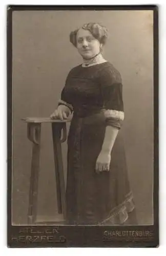 Fotografie Atelier Herzfeld, Charlottenburg, Wilmersdorferstrasse 56, Frau in elegantem Kleid neben Tisch