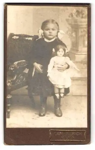 Fotografie Carl Ullrich, Mügeln, Junges Mädchen mit Schleifen im Haar und ihrer Puppe im Arm