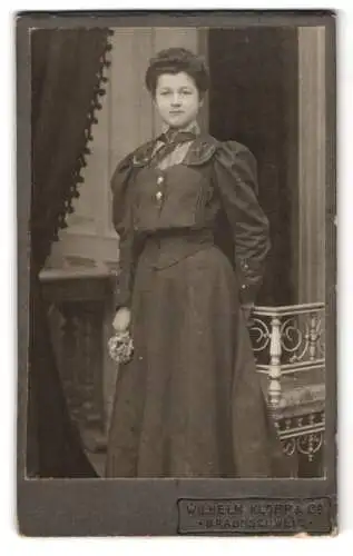 Fotografie Wilhelm Klopp & Co., Braunschweig, Eine Frau in einem eleganten Kleid mit Blumenstrauss