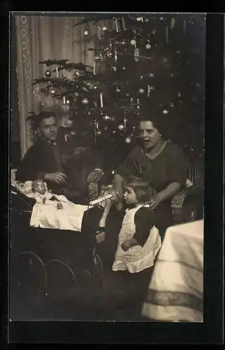 Foto-AK Kleines Mädchen mit ihren Eltern und einem Puppenwagen am Weihnachtsbaum