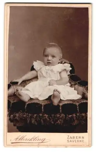 Fotografie A. Merckling, Zabern, Sitzendes Baby in weissem Kleid