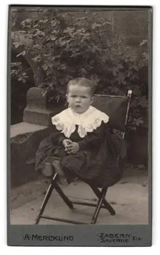 Fotografie A. Merckling, Zabern, Ein kleines Kind auf einem Klappstuhl in einem Garten