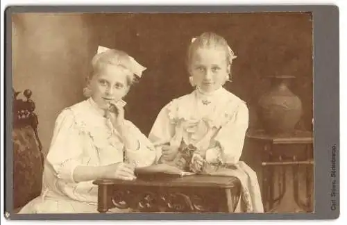 Fotografie Carl Stüwe, Süderbrarup, Zwei junge Mädchen an einem Tisch mit Buch