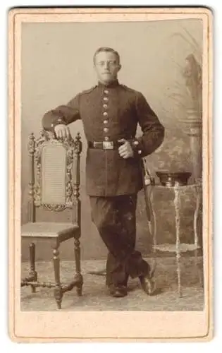 Fotografie E. Bremen, Metz-Sablon, Kaiser-Wilhelmstrasse 37, Soldat in Uniform neben Stuhl und Tischchen