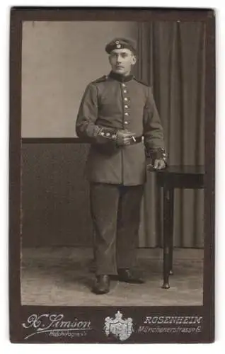 Fotografie X. Simson, Rosenheim, Münchenerstrasse 6, Soldat in Uniform neben einem Tisch