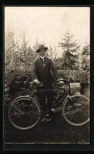 Foto-AK Ein junger Mann im Anzug mit seinem Fahrrad vor einer alten Mauer