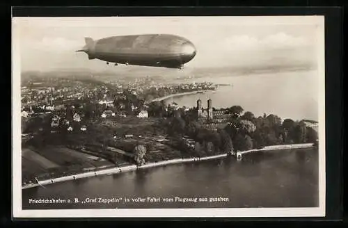 AK Friedrichshafen, Graf Zeppelin in voller Fahrt über dem Ort am Ufer des Bodensees, Luftschiff