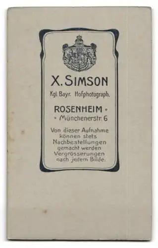 Fotografie X. Simson, Rosenheim, Münchenerstrasse 6, Soldat in Uniform neben Tisch mit Uhr