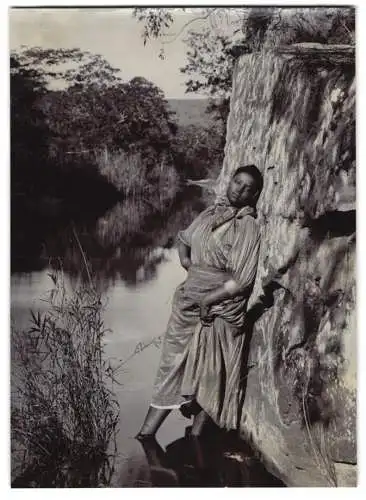 Fotografie Afrika, junge afrikanische Frau am Felsen in einem Fluss lehnend