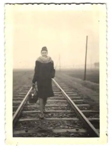 Fotografie junge Dame im Mantel mit Pelzbesatz spaziert Eisenbahn-Gleise entlang