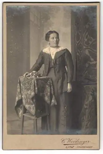 Fotografie C. Weidinger, Linz, Promenade 3, Dame in elegantem Kleid neben dekorativem Tisch