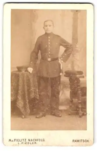 Fotografie M.v. Fielitz Nachfolg., Rawitsch, Berlinerstr. 190, Ein Soldat in Uniform stehend neben einem Tisch