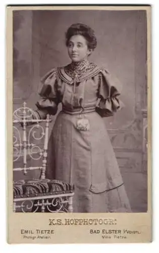 Fotografie Emil Tietze, Bad Elster i. Voigtl., Frau in elegantem Kleid an einem dekorativen Stuhl