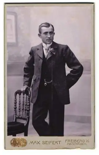 Fotografie Max Seifert, Freiberg i. S., Poststrasse 11, Eleganter Herr im Anzug, stehend mit einer Hand auf einem Stuhl