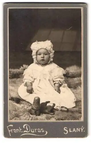 Fotografie Frant. Duras, Slany, Husova Trida 93, niedliches Baby mit Haube und Spielzeug