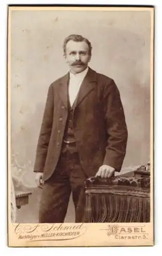 Fotografie C. F. Schmid, Basel, Clarastr. 5, Eleganter Herr mit Schnurrbart neben einem Tisch