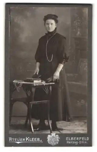 Fotografie Atelier Kleeb, Elberfeld, Herzog-Strasse 4, Dame in schwarzem Kleid neben Tisch