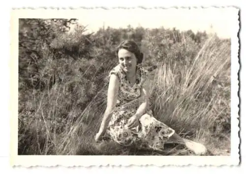 Fotografie junge Brünette Frau mit Sommerkleid zwischen Gräsern sitzend