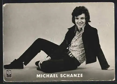 AK Musiker Michael Schanze sitzt lächelnd auf dem Boden, mit Autograph