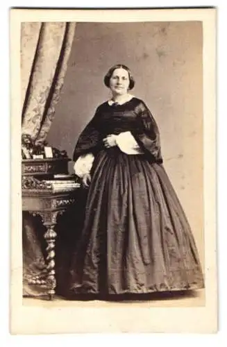 Fotografie H. Reuter, Braunschweig, Südliche Wilhelmstrasse 88, Frau in elegantem Kleid neben Tisch