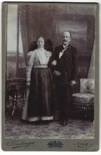 Fotografie C. Weidinger, Linz, Promenade 3 Mohren, Dame in Tracht nebst Herr im Anzug mit Ansteckblumen