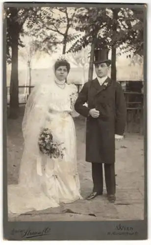 Fotografie Strauss & Co., Wien, junges Brautpaar im Hochzeitskleid und im Anzug mit Zylinder