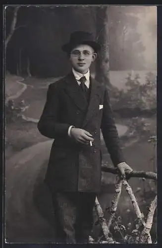 Foto-AK Junger Mann im Anzug mit Zigarette vor Studiokulisse