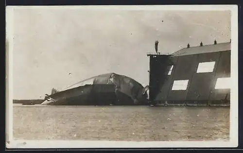 AK Beschädigter Zeppelin auf dem Wasser vor einem Luftschiffhafen