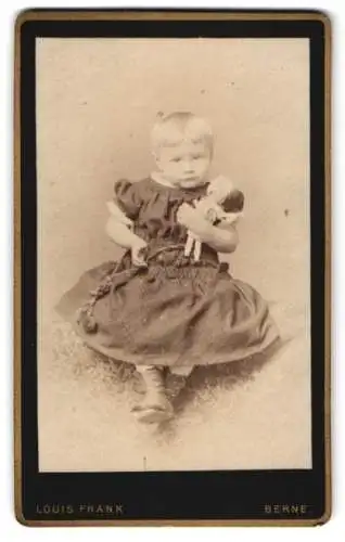 Fotografie Louis Frank, Berne, niedliches kleines Mädchen im Kleid mit ihrer Puppe im Arm